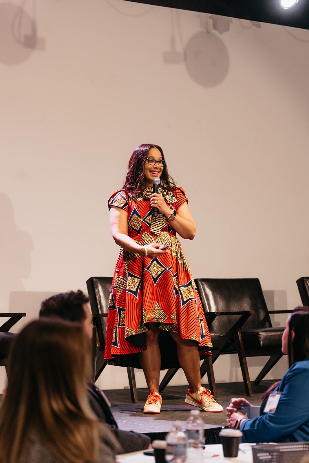 Kelli Williams delivering a keynote on stage in an orange dress